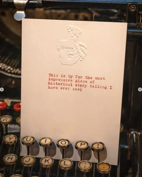A postcard with an embellished logo and red ink between the keys of a typewriter. The note reads: 'This is by far the most impressive piece of historical storytelling I have ever seen.'