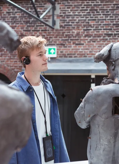 A visitor looks enraptured at a statue with his audio head set on.