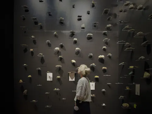 An older woman looks up to a black wall filled with seemingly floating stones on display.