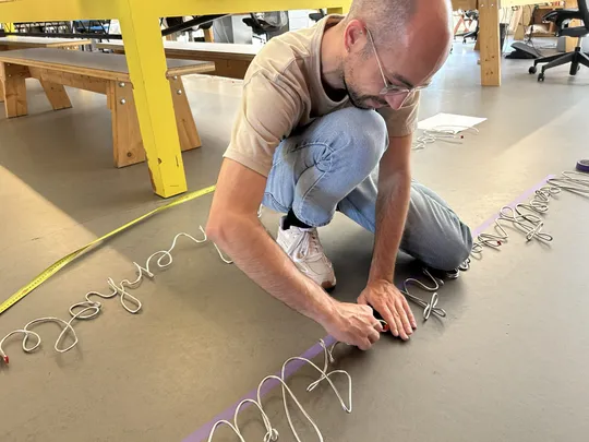 Lead designer Robin bends the finishing touches to one of the iron quotes on the floor, next to KDJ's yellow lunch table.