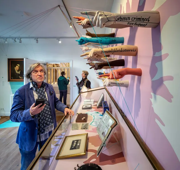 Plastic arms mounted on the wall in diverse colours, pointing at the visitors.